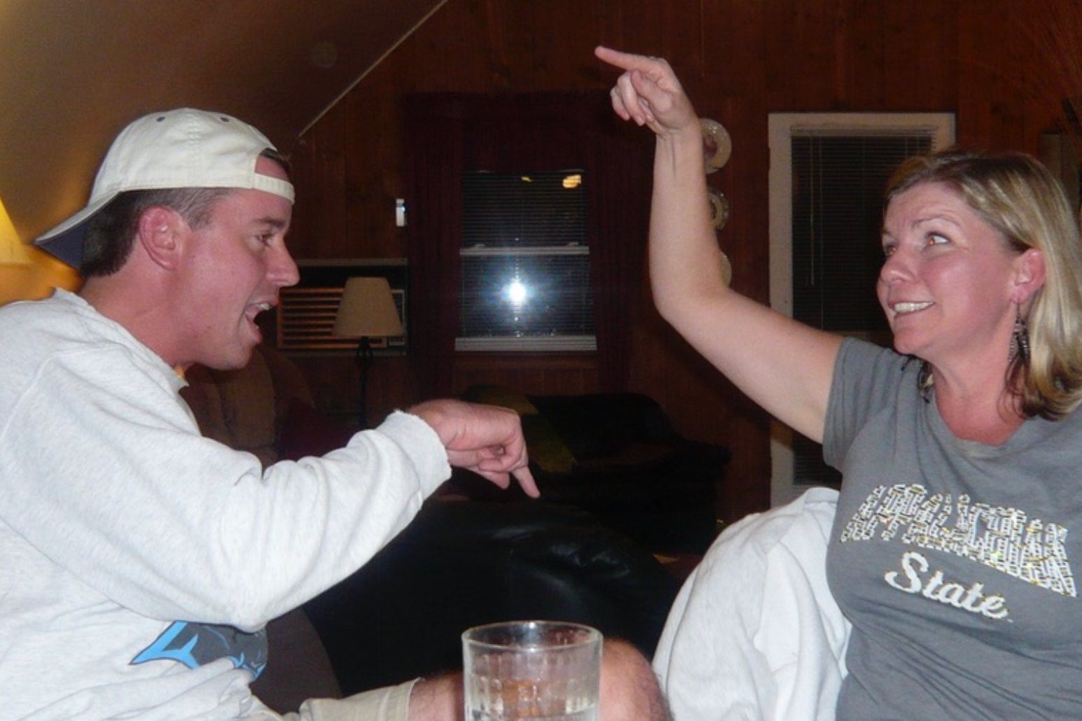 Seth in a backwards cap and Donna pointing at each other, laughing during a family game of Apples to Apples