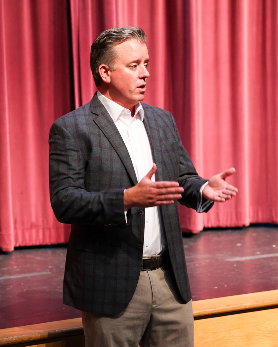 Seth Marlowe speaking on stage in front of a red curtain